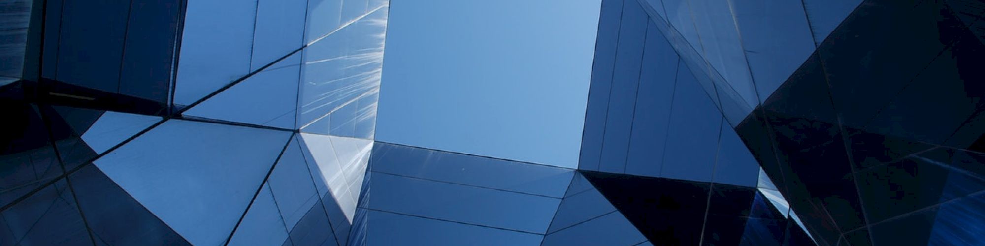 Abstract view of mirrored geometric structures forming a skylight with reflections, creating a dynamic architectural perspective.