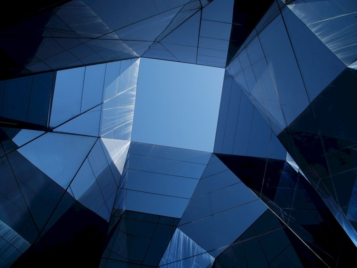 Abstract geometric architecture with reflective glass surfaces forming a complex pattern against a blue sky backdrop.