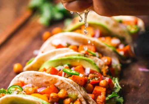 Tacos with veggies, chickpeas, avocado, onion; lime being squeezed over them on a wooden board.