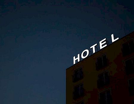 A hotel building at night features a bright, illuminated "HOTEL" sign on its roof against a dark sky.