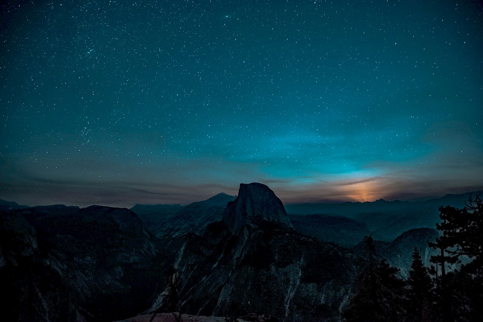 Starry night sky over a mountainous landscape with a prominent peak silhouetted, creating a serene and majestic view.