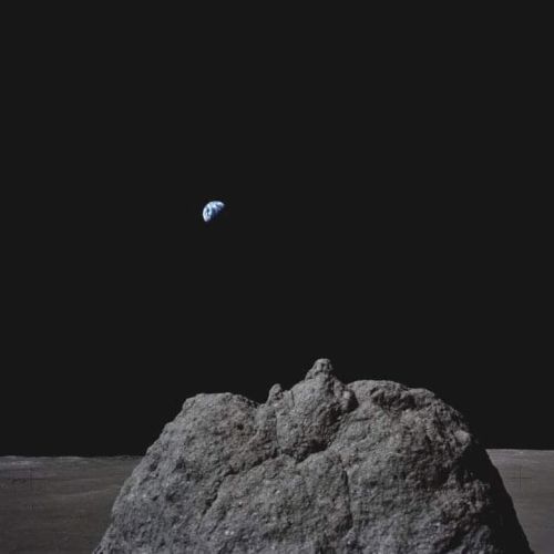 A rocky foreground with Earth visible in the distant sky over a dark background, resembling a view from the lunar surface.