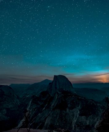 A starry night sky over a mountainous landscape with a glowing horizon and silhouetted peaks in the foreground.