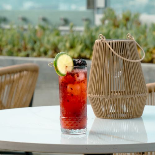 A vibrant drink with berries and a lime slice on a table, next to a wooden lantern with a scenic background.