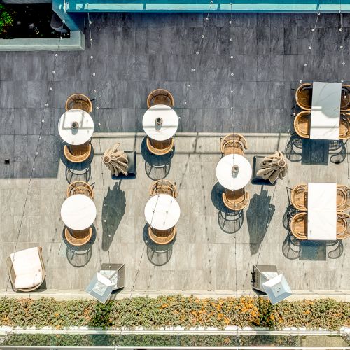 Aerial view of an outdoor patio with arranged tables, chairs, and loungers, surrounded by greenery and a blue pergola.