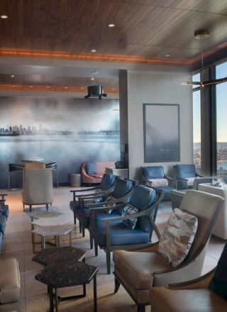 A modern lounge with chairs and tables, featuring large windows with a scenic view and a mural on the wall, provides a relaxed atmosphere.
