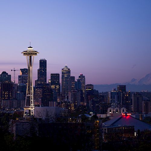 The image shows a city skyline at dusk with a prominent tower and a mountain in the background under a purple sky.