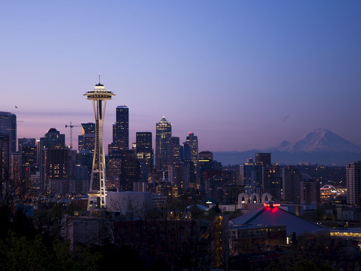 Seattle skyline at dusk with the Space Needle prominently visible, and Mount Rainier faintly in the background.