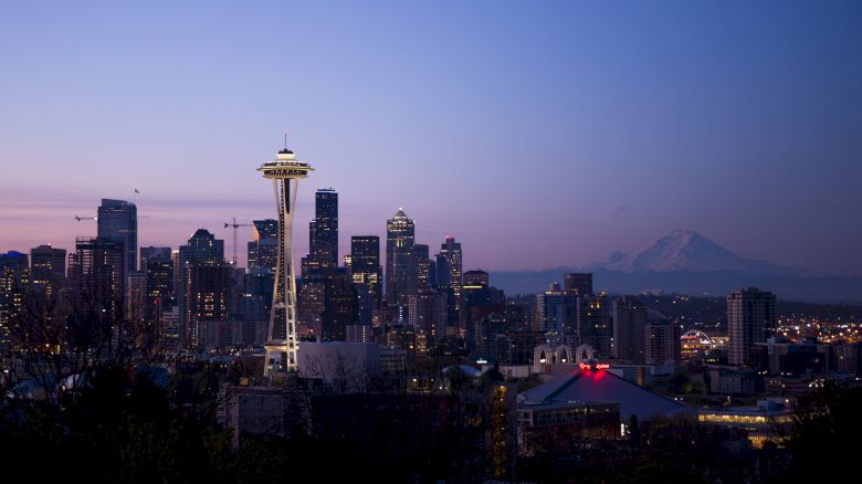 Seattle skyline at dusk with the Space Needle prominently visible, and Mount Rainier faintly in the background.