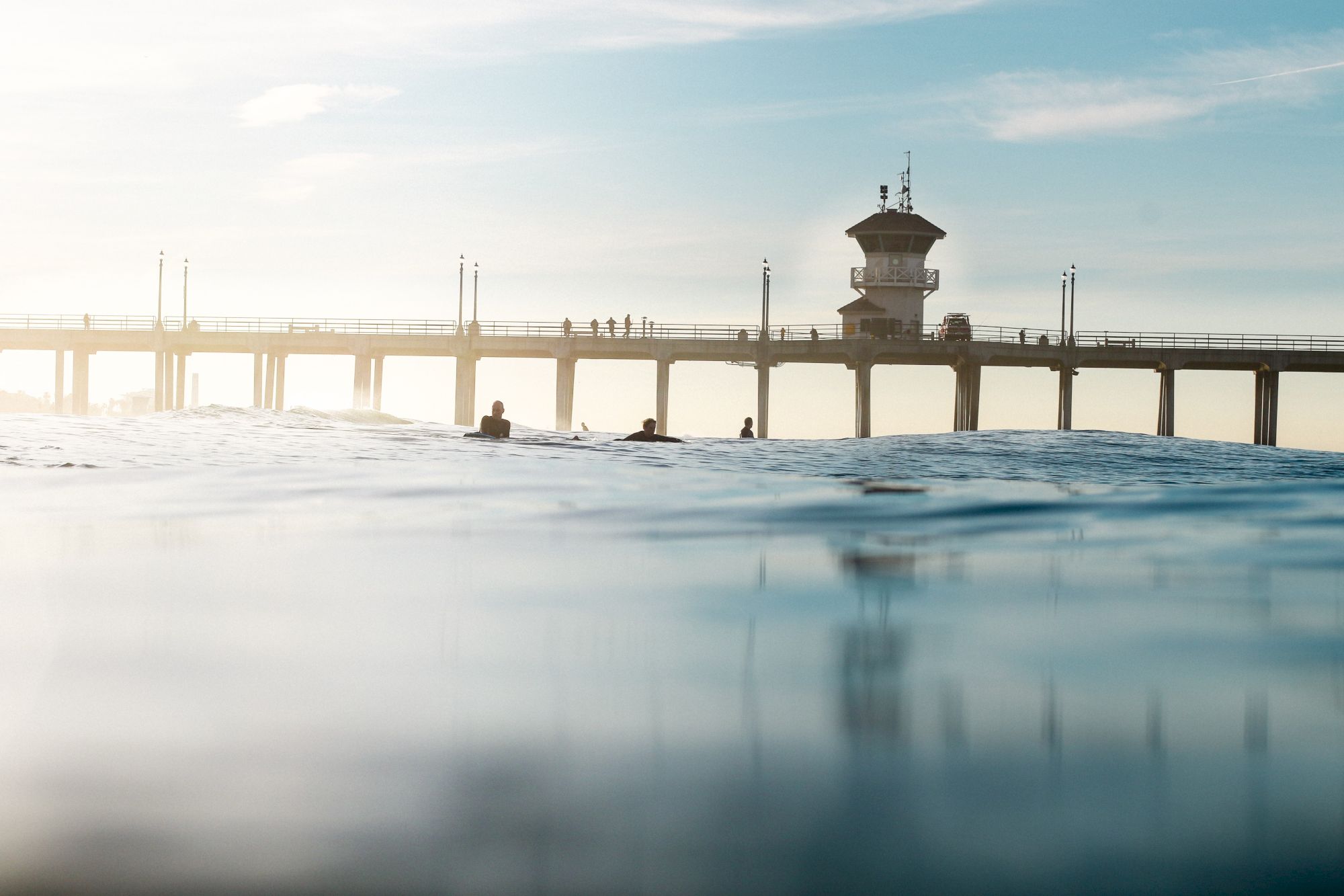 A serene seascape showing a pier extending into the ocean with people walking atop, and the foreground focus on gentle water ripples.